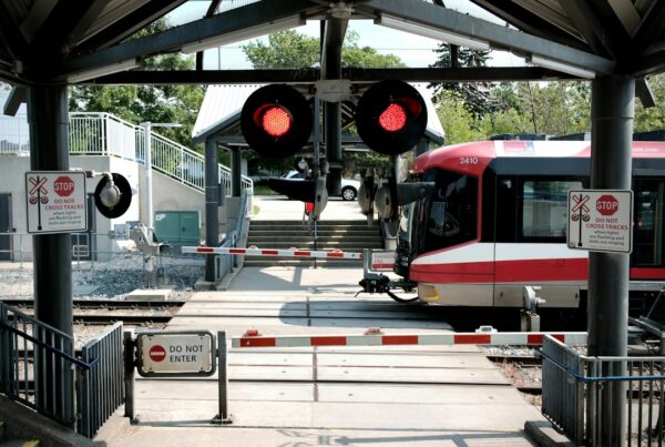 Railway level crossing with barriers lowered and red warning lights flashing as a train approaches