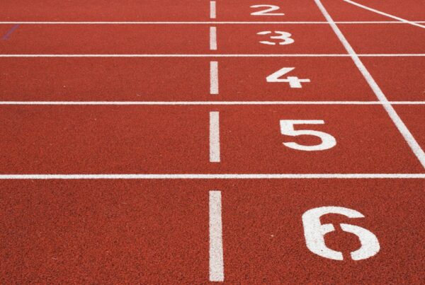 A red running track with white lane lines and painted lane numbers at the start line