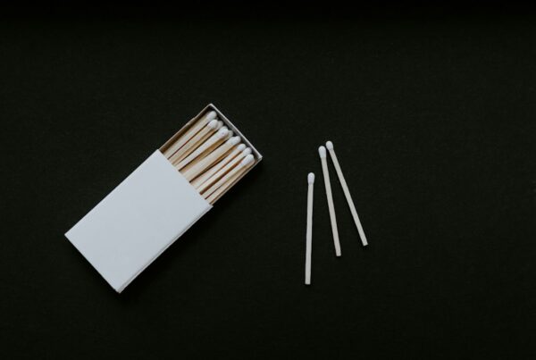 An open box of unstruck matches with three matchsticks laid beside it on a dark background