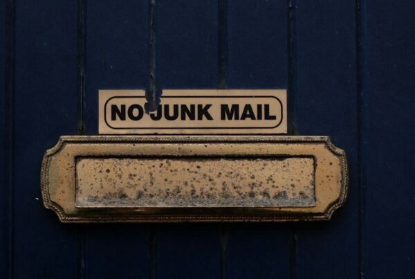 A brass letterbox on a dark blue door with a NO JUNK MAIL sign fixed above the slot