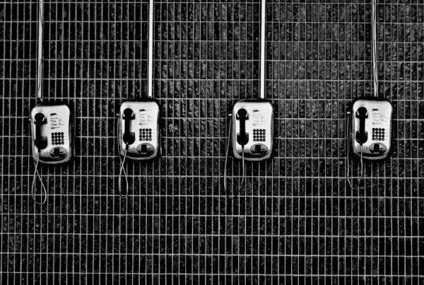 Four identical black and grey payphones mounted in a row on a tiled wall