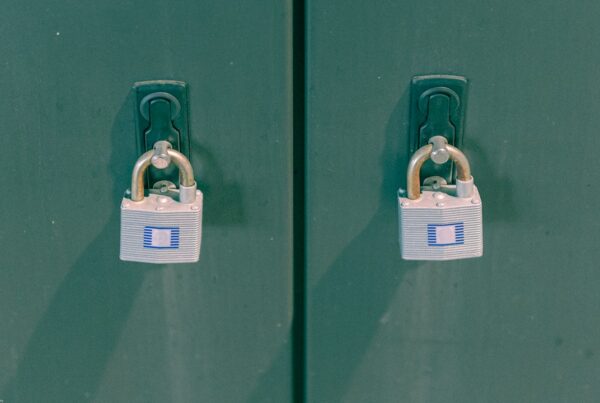Two identical padlocks fastened to the hasps of two green metal locker doors, photographed from outside