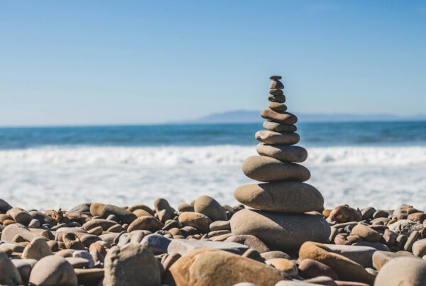 A stack of smooth pebbles balanced on a shingle beach, with the sea behind it