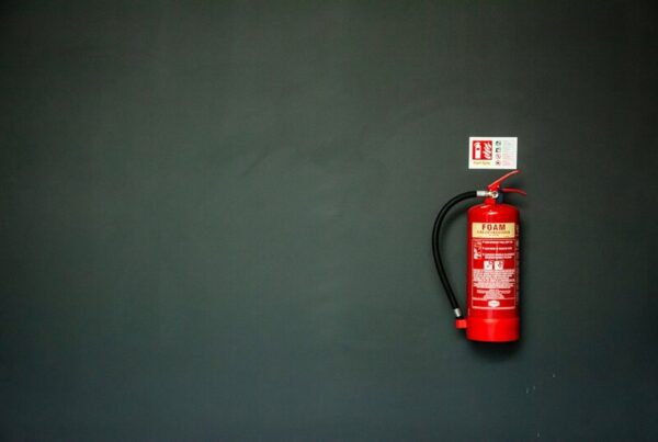 A single red foam fire extinguisher mounted on a bare dark green wall beneath its small safety sign, with empty wall on either side.